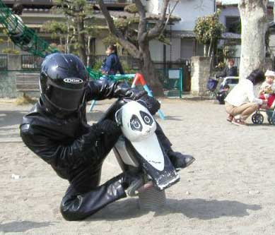 man in playground in leathers and helmet on toy motorbike